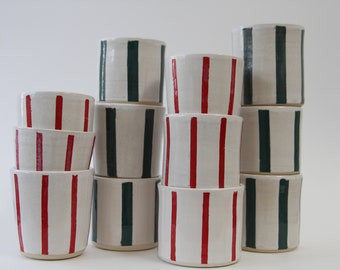 May include: A stack of ceramic mugs with red and green stripes. The mugs are white with red or green stripes painted on them.