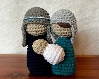 May include: Two crocheted figures, one in teal and one in navy blue, wearing gray hats. The figures are holding a white crocheted ball.