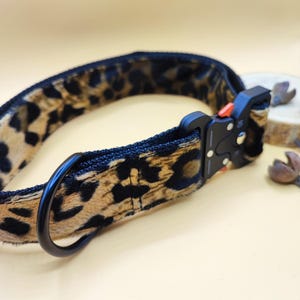 Könnte beinhalten: Ein schwarzes und braunes Hundehalsband mit Leopardenmuster, einer schwarzen Metallschnalle und einem schwarzen Metall-D-Ring.