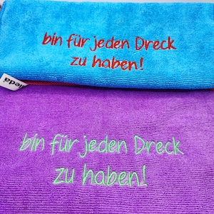 Könnte beinhalten: Zwei Mikrofasertücher, eines in Türkis und eines in Lila. Das türkisfarbene Tuch hat einen roten gestickten Text, der lautet: "bin für jeden Dreck zu haben!". Das lila Tuch hat einen grünen gestickten Text mit demselben Wortlaut.
