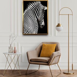 May include: A black and white zebra print framed artwork hanging on a white wall above a brown armchair with a yellow pillow. A gold floor lamp with a white globe shade is in the corner of the room.