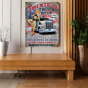 May include: A vintage-style metal sign with a red, white, and blue color scheme. The sign advertises "Trixie's Truck Stop" with a cartoon image of a woman in a red, white, and blue bikini standing next to a semi-truck. The sign also includes the text "Truckers Drive America", "Full Service 24 Hours", "Road Girls Garage", and "No Problem Too Big To Handle".