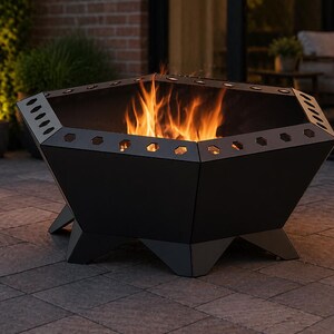 May include: A black, geometric fire pit with flames burning inside. The fire pit has a hexagonal shape with cut-out details around the top edge. It sits on a patio, with plants and a brick wall in the background.