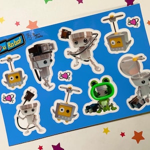 May include: A sheet of stickers with a blue background featuring various robot designs. The robots are primarily silver and gray, with some having yellow or green accents. The phrase "I ❤️ U Robots!" is printed on the sheet.