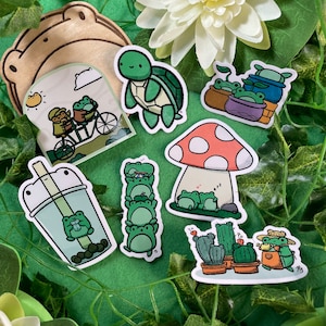 May include: A set of nine frog-themed stickers featuring a variety of designs, including a frog riding a bicycle, a frog in a bubble tea cup, a frog wearing a mushroom hat, and a frog sitting on a cactus. The stickers are perfect for adding a touch of whimsy to your planner, laptop, or water bottle.