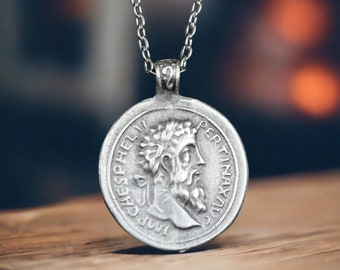May include: A silver chain necklace with a round pendant featuring a profile of a man with a beard and a crown. The pendant has the text "IMP CAES PHELI" and "PERTINAX AUG" around the edge.