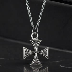 May include: A silver chain necklace with a silver cross pendant. The cross has a detailed design with small dots around the edges.