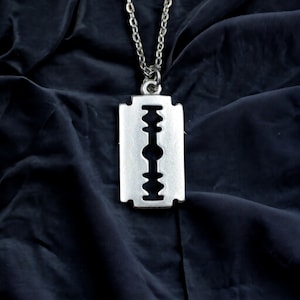 May include: A silver chain necklace with a razor blade pendant. The pendant is a realistic depiction of a razor blade with a sharp edge.