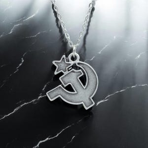 May include: A silver necklace with a pendant shaped like a hammer and sickle with a star on top.