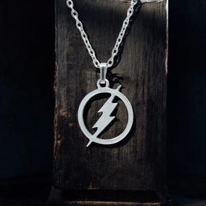 Könnte beinhalten: Silberne Halskette mit einem runden Anhänger, der ein Blitzsymbol zeigt.