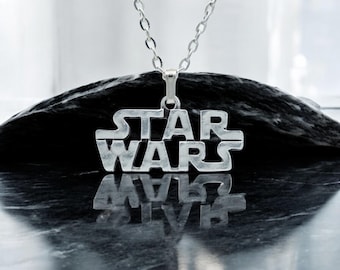 May include: A silver necklace with a Star Wars logo pendant. The pendant is a cutout of the Star Wars logo, with the words "STAR WARS" written in a bold, blocky font.