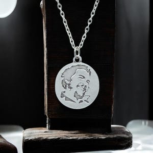 May include: A silver necklace with a round pendant featuring a detailed profile of a person's face.