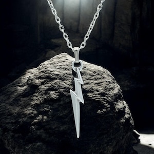 May include: A silver chain necklace with a lightning bolt pendant. The pendant is a stylised lightning bolt with a pointed tip.