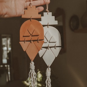 May include: Two ceramic wall hangings with geometric shapes and tassels. One is terracotta orange and the other is white.