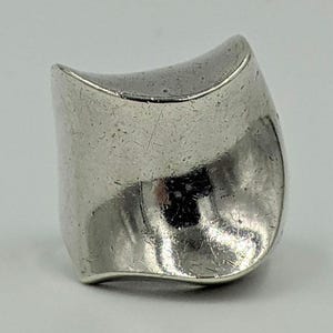 May include: A silver ring with a unique, curved, and slightly asymmetrical design. The ring has a smooth, polished finish and a slightly textured surface.