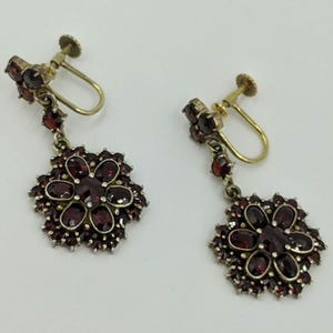 May include: A pair of dangle earrings with a floral design. The earrings are made of silver and feature red garnet stones.