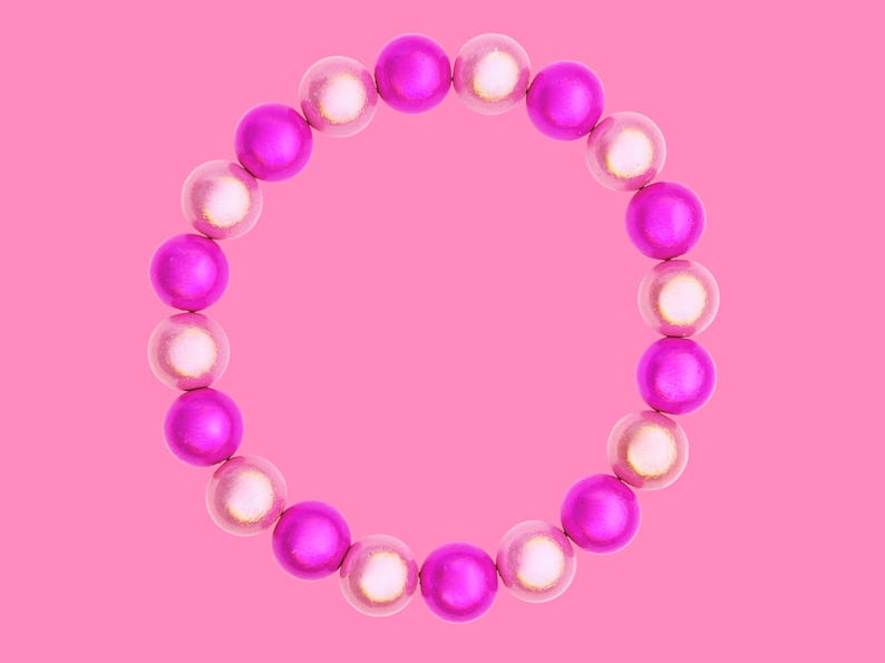 A circular bracelet made of alternating pink and white beads is displayed against a solid pink background.