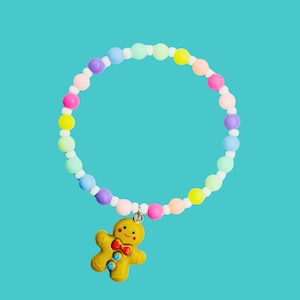 May include: A vibrant beaded bracelet with a gingerbread man pendant. The bracelet is made up of pastel-coloured beads in shades of pink, yellow, green, blue, and purple. The gingerbread man charm is yellow with a red bow.