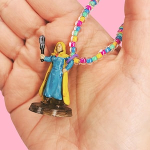 May include: A miniature figurine of a robed figure in blue and yellow, holding a weapon, on a brown base. A colorful beaded necklace with rainbow beads is also present.