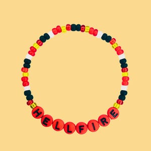 Pode incluir: Uma pulseira de contas com a palavra "HELLFIRE" escrita em contas de letras vermelhas. A pulseira apresenta um padrão de contas vermelhas, pretas, brancas e amarelas. O fundo é amarelo claro.