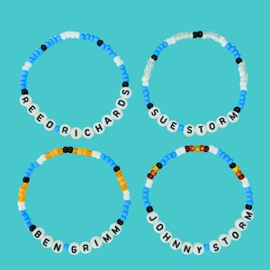 May include: Four beaded bracelets with white letter beads spelling out names against a teal background. The bracelets are blue, white, black, and orange. The names are Reed Richards, Sue Storm, Ben Grimm, and Johnny Storm.