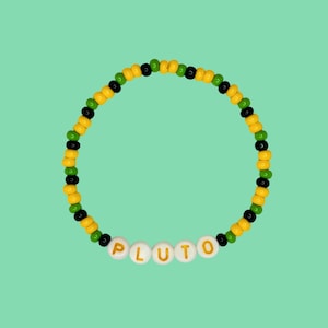 Può includere: Un braccialetto di perline gialle, verdi e nere con la parola "PLUTO" scritta in perline bianche con lettere dorate.