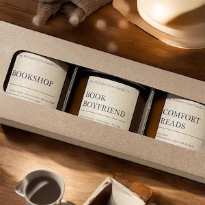 May include: A gift set of three scented candles in a cardboard box. Each candle has a label with a unique name: "Bookshop", "Book Boyfriend", and "Comfort Reads". The labels include scent descriptions. The candles are in glass jars.