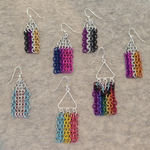 May include: Six pairs of dangle earrings with chainmail designs in various colors, including black, white, gray, pink, blue, purple, yellow, orange, and green. The earrings are made with silver-toned metal.