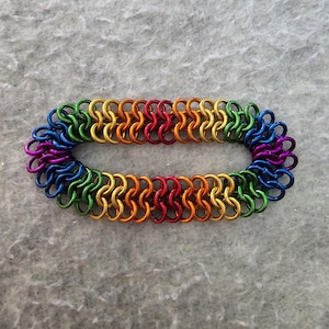 May include: A rainbow colored chainmail bracelet made of small metal rings. The bracelet is made in a pattern that resembles a chain.