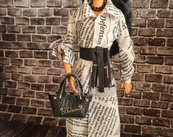 May include: A fashion doll wearing a white and black newspaper print dress with a black belt and a black purse that says "Princess" on it. The doll has long black hair and is wearing a black necklace.