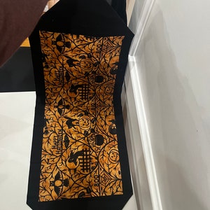 May include: Black table runner with a gold and black Halloween design. The design features owls, pumpkins, bats, and the words "Happy Halloween" and "Boo".