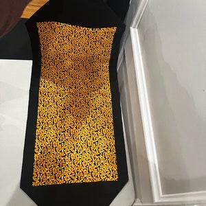 May include: Black table runner with a pattern of orange and white candy corn. The runner has a pointed end.