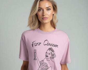 Puede incluir: Una camiseta rosa con un dibujo en línea negra de una mujer con una corona y sosteniendo una copa de champán. El texto "Fizz Queen" está escrito encima del dibujo.