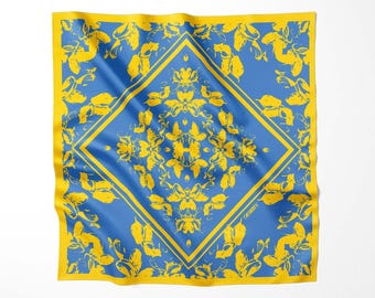May include: A square scarf featuring a vibrant yellow and blue color scheme. The design includes a central diamond frame filled with symmetrical floral patterns, surrounded by a yellow border and yellow leaf motifs on a blue background.