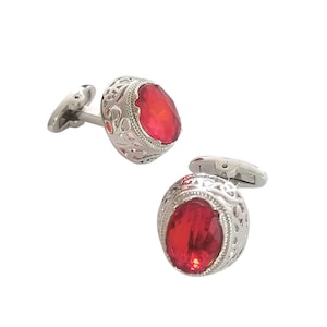 May include: A pair of silver cufflinks with red gemstone accents. The cufflinks feature an intricate, filigree design.