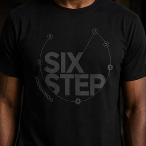 May include: A black short-sleeved t-shirt featuring a dark grey graphic print. The design displays the text SIX STEP in large capital letters, surrounded by a circular path marked with numbers one through six and the word DOWNROCK.