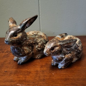 May include: Two ceramic rabbit figurines, one larger than the other. Both are brown and white with a speckled glaze.