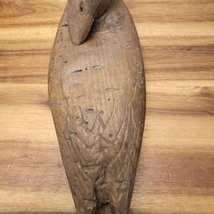 May include: A carved wooden duck sculpture with a detailed design. The duck is brown with carved feather details and a curved neck. The sculpture is placed on a wooden surface.