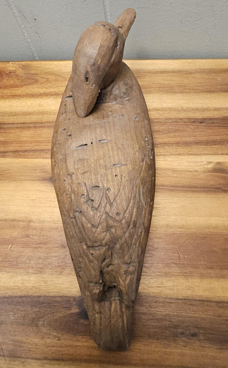 May include: A carved wooden duck sculpture with a detailed design. The duck is brown with carved feather details and a curved neck. The sculpture is placed on a wooden surface.
