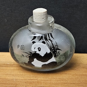 May include: A clear glass bottle with a white stopper. The bottle features a hand-painted panda bear design in black and white, with bamboo stalks. The Chinese characters for "China" are also visible.