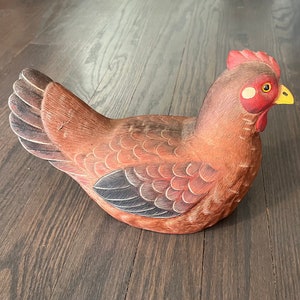 Könnte beinhalten: Eine geschnitzte Holzfigur eines Huhns mit brauner, roter und schwarzer Farbe. Das Huhn hat ein detailliertes Design mit Schuppen und Federn.