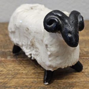 May include: A ceramic figurine of a ram with a white, crackled glaze body and a smooth, solid black head featuring curved horns. The ram stands on four black legs, with the textured white wool finish showing a distinct network of fine cracks.