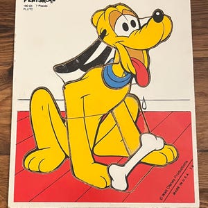 以下が含まれることがあります： ヴィンテージのプレイスクールプルートパズル。黄色い漫画の犬は赤い舌と白い骨を持っています。パズルは赤と白の背景にあり、7つのピースがあります。「ウォルト・ディズニー・プロダクションズ」と「メイド・イン・USA」の文字が見えます。