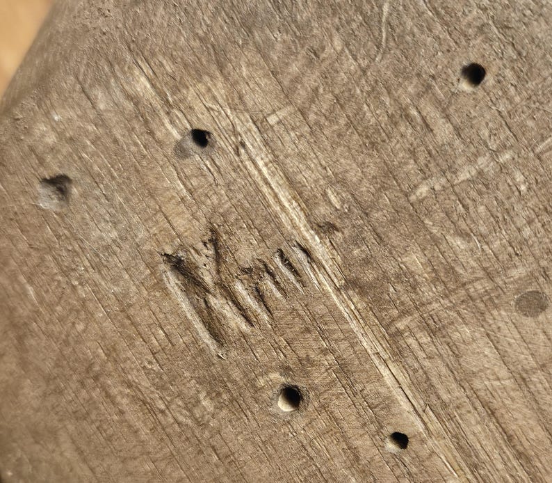 May include: Close-up of a weathered wooden surface with visible grain and several small, dark holes. The word "Kimi" is carved into the wood. The wood has a natural, light brown color.