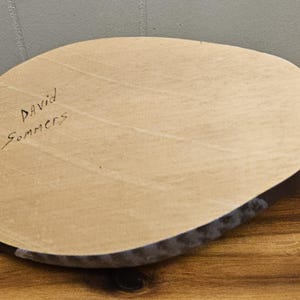 May include: A wooden duck decoy with a light brown oval-shaped top and a black body. The text "David Sommers" is handwritten on the top. The decoy has a gray tail.
