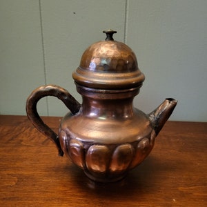 May include: A copper teapot with a domed lid and a decorative, scalloped design. The teapot has a handle and a spout.