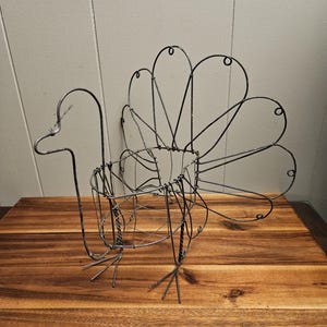 May include: A wire turkey sculpture with a round body and a long neck. The turkey has a fan-shaped tail and wire legs.