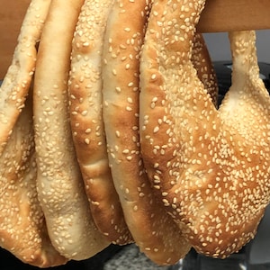 May include: A close-up of five round, sesame seed covered breads hanging on a wooden rack. The breads are light brown in color and have a slightly crispy texture.
