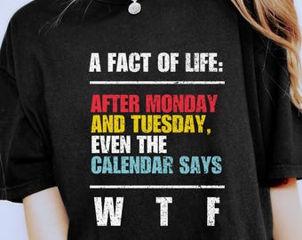 May include: Black t-shirt with the text "A FACT OF LIFE: AFTER MONDAY AND TUESDAY, EVEN THE CALENDAR SAYS WTF" in white, red, yellow, and blue. The shirt is worn with leopard print shorts.