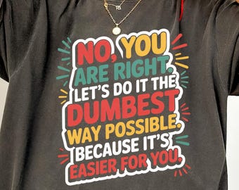 May include: Dark gray t-shirt with the text "NO YOU ARE RIGHT LET'S DO IT THE DUMBEST WAY POSSIBLE BECAUSE IT'S EASIER FOR YOU" in a colorful, playful design. The shirt has short sleeves and a relaxed fit.